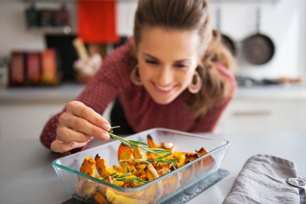 Glücklich über ihre überbackenen Kürbisscheiben garniert eine Frau noch die Speise mit Gewürzen | Credit: iStock.com/CentralITAlliance