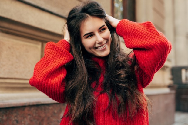 Gut gelaunte junge Frau in rotem Pullover fährt sich durchs Haar | Credit: iStock.com/Yuricazac
