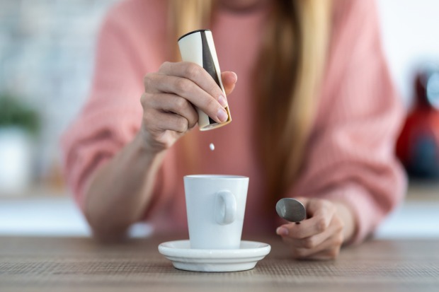 Frau gibt aus einem Spender Süßstoff in eine Kaffetasse