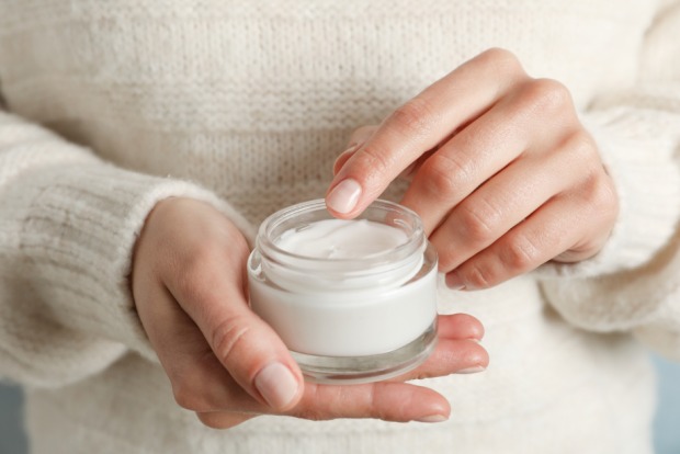 Frau hält einen offenen Creme-Tegel in ihrer Hand | Credit: iStock.com/AtlasStudio