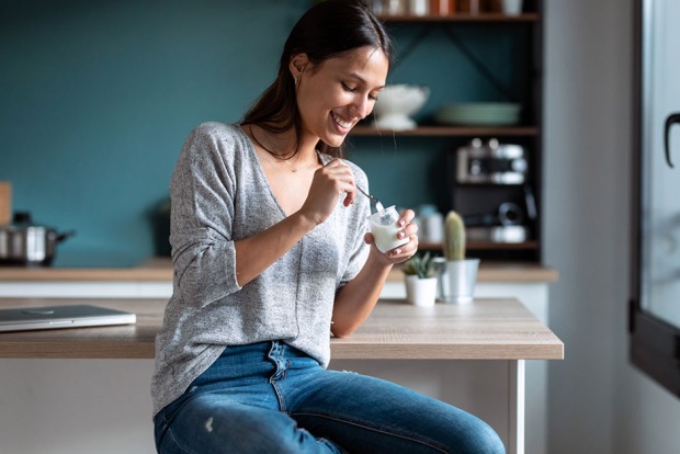 Junge Frau genießt ein Joghurt in ihrer Küche | Credit: iStock.com/nensuria