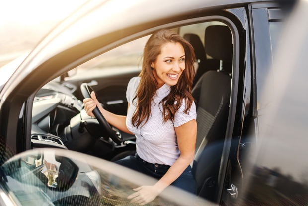 Bei offener Autotür sitzt eine junge Frau lächelnd hinter dem Steuer | Credit: iStock.com/dusanpetkovic