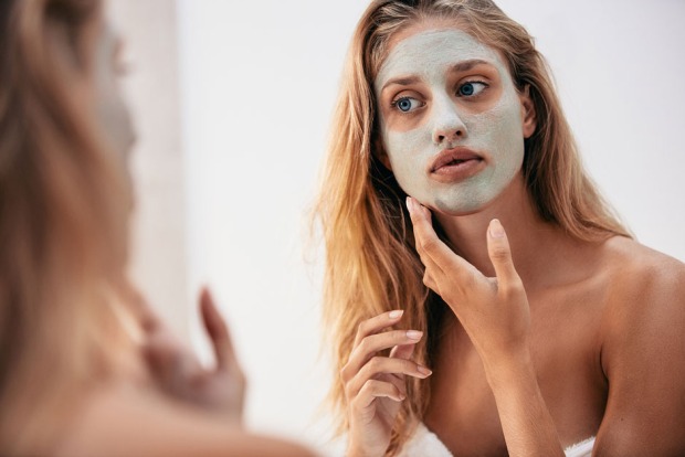 Junge Frau trägt sich eine Gesichtsmaske auf | Credit: iStock.com/Jacob Ammentorp Lund
