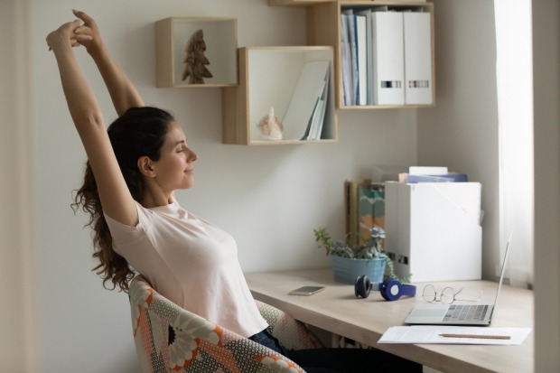 Frau sitzt vor Schreibtisch und streckt sich | Credit: iStock.com/fizkes