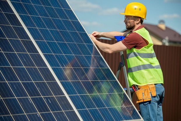 Monteur befestigt Solarmodule auf einem Dach | Credit: iStock.com/shironosov