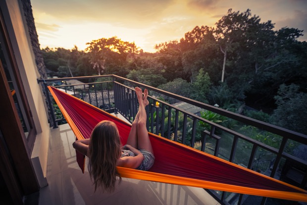 Junge Frau in ihrer Hängematte auf dem Balkon an einem lauen Sommerabend | Credit: iStock.com/mihtiander