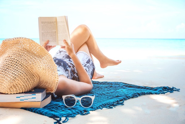 Junge Frau beim Lesen am Strand bei Sonnenschein | Credit: iStock.com/Yumi mini