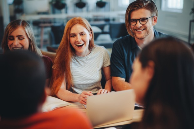 Fröhliche Runde junger Menschen, die vor ihren Notebooks sitzen | Credit: iStock.com/jacoblund