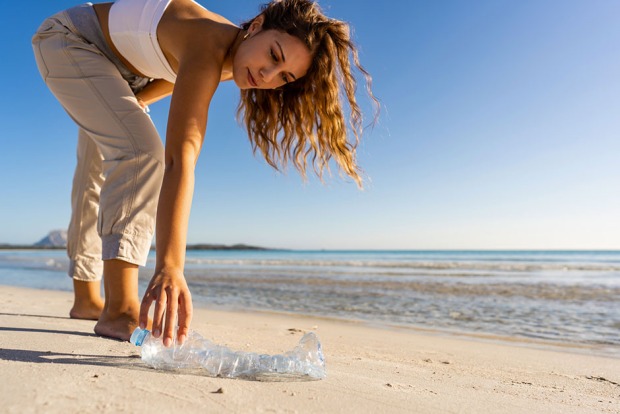 Junge Frau sammelt am Strand Plastikmüll ein | Credit: iStock.com/Robby Fontanesi