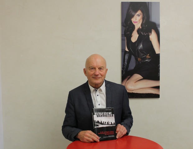 Valentin Hauser steht in einen Anzug gekleidet und mit seinem neuen Buch in der Hand hinter einem roten Stehtisch