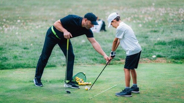 Golflehrer zeigt Bub wie das Golfen geht. | Credit: iStock.com/microgen