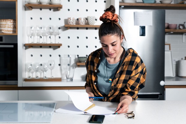Junge Frau in der Küche mit ihrer Checkliste | Credit: iStock.com/Srdjanns74