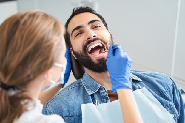 Zahnärztin untersucht einen Mann | Credit: iStock.com/YakobchukOlena