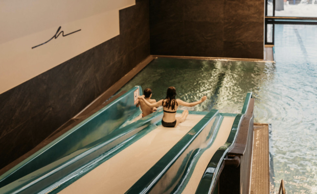 Zwei Kinder rutschen in den Indoorpool.