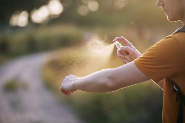 Junger Mann sprayt Insektenschutzmittel auf seinen Arm. | Credit: iStock.com/Chalabala