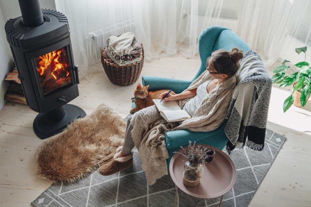 Frau sitzt in einem Sessel vor einem Ofen | Credit: iStock.com/perfectlab