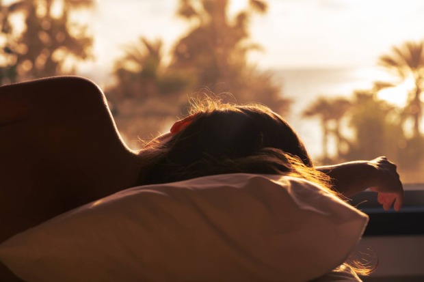 Junge Frau schläft in ihrem Bett bei Sonnenaufgang | Credit: iStock.com/FTiare