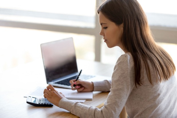 Junge Frau vor ihrem Notebook mit Taschenrechner | Credit: iStock.com/fizkes