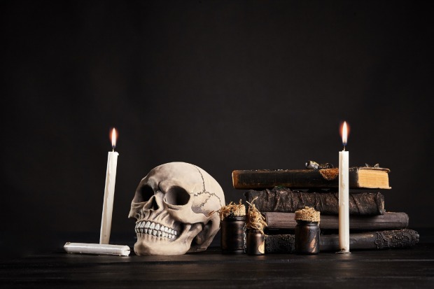 Totenkopf steht mit Kerzen auf einem schwarzen Tisch | Credit: iStock.com/Sergey Nazarov