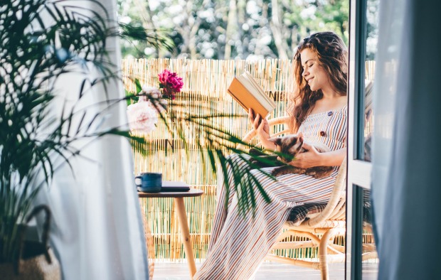 Frau sitzt am Balkon und liest | Credit: iStock.com/Maria Korneeva