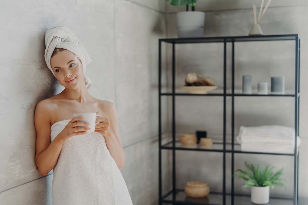Frau steht im Badezimmer mit einer Kaffee-Tasse in der Hand | Credit: iStock.com/Viorel Kurnosov