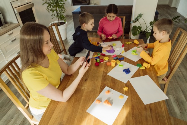 Während die Kinder zeichnen, schaut die Mutter in ihr Smartphone.
