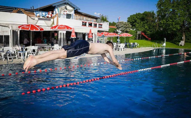 Mann springt im Freibad ins Wasser.