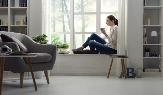 Frau sitzt gemütlich auf einer Fensterbank | Credit: iStock.com/demaerre