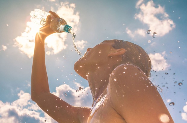 Frau gießt sich Wasser aus der Flasche über ihren Kopf an heißen Tagen | Credit: iStock.com/kieferpix