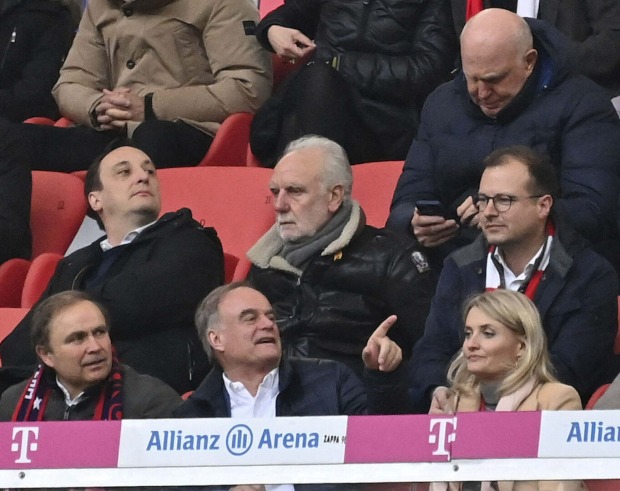 Franz Beckenbauer sitzt mit anderen Männern im Fußballstadion.