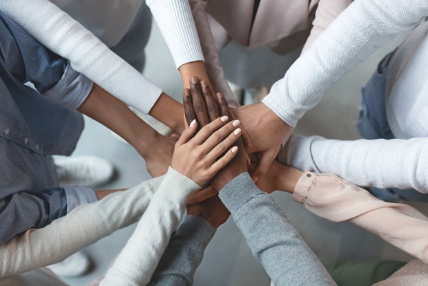 Junge Menschen unterschiedlicher Kulturen stehen im Kreis und legen die Hände übereinander | Credit: iStock.com/Prostock-Studio