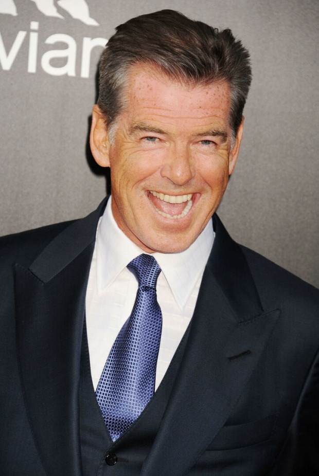 Pierce Brosnan lächelt verschmitzt in die Kamera und trägt einen Anzug mit Krawatte.