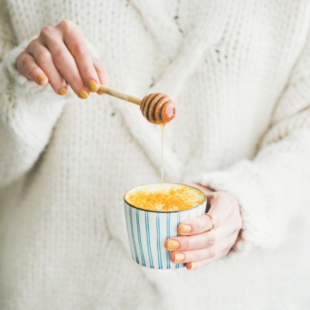 Golden Milk in der Tasse, Frau fügt Honig hinzu
