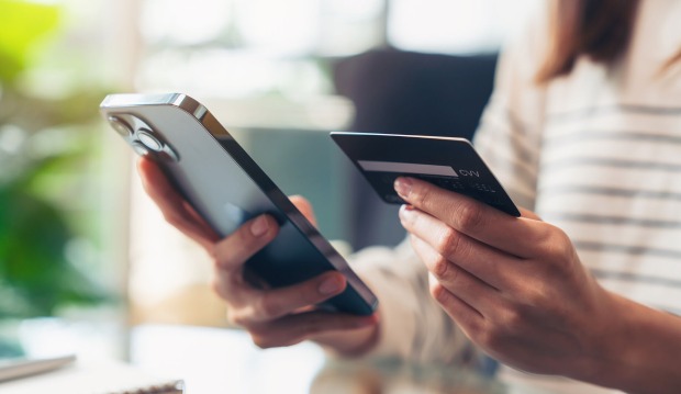 Eine Frau, die ein Smartphone sowie eine Kreditkarte in Händen hält