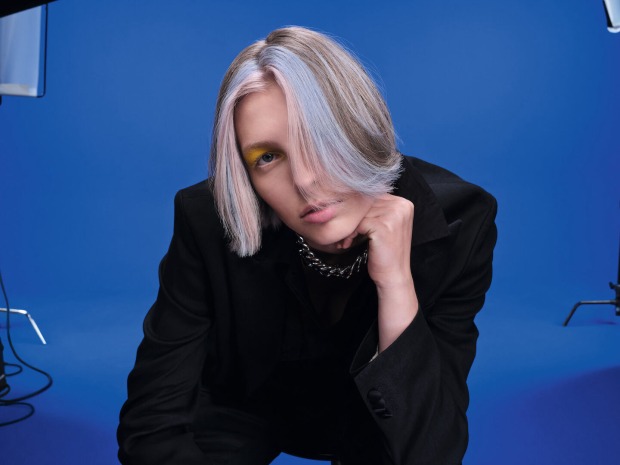 ein Mann mit mittellangen Haaren und blauen Strähnen vor einer blauen Fotowand
