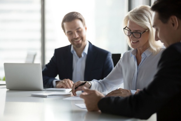 Zwei Männer und eine Frau bei einer Vertragsunterzeichnung | Credit: iStock.com/fizkes