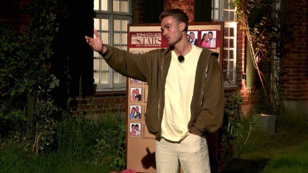 Sommerhaus der Stars Teilnehmer Can bei der Nominierung. Er trägt einen olivgrünen Pulli und ein gelbes T-Shirt.