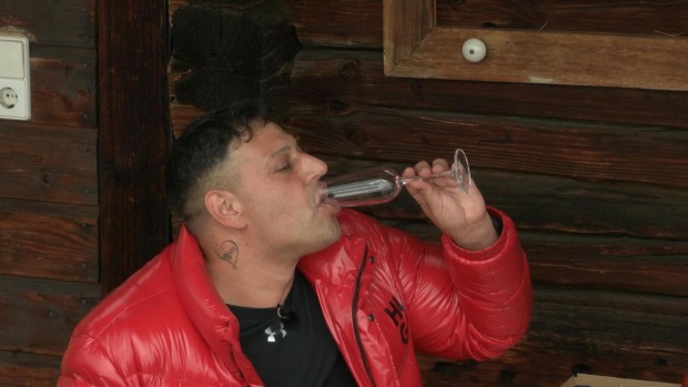 Marius trägt ein rote dicke Winterjacke und trinkt aus einem Glas Sekt.