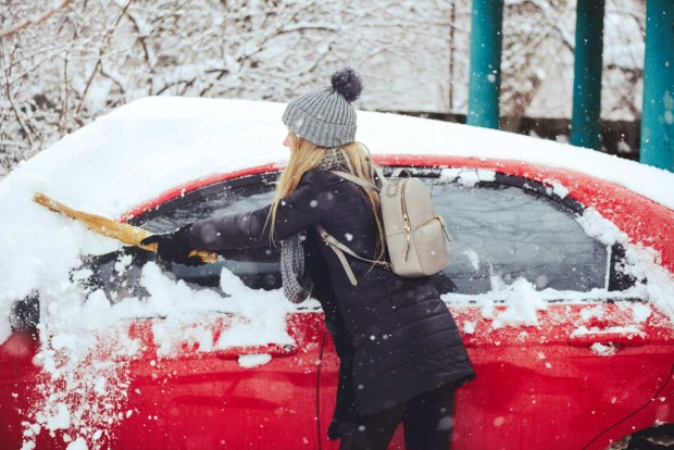 Eine Frau befreit ihr rotes Auto von Schnee.