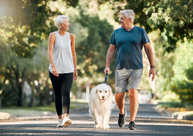 Ein älteres Liebespaar das mit im sportlichen Outfit mit einem Hund spazieren geht.