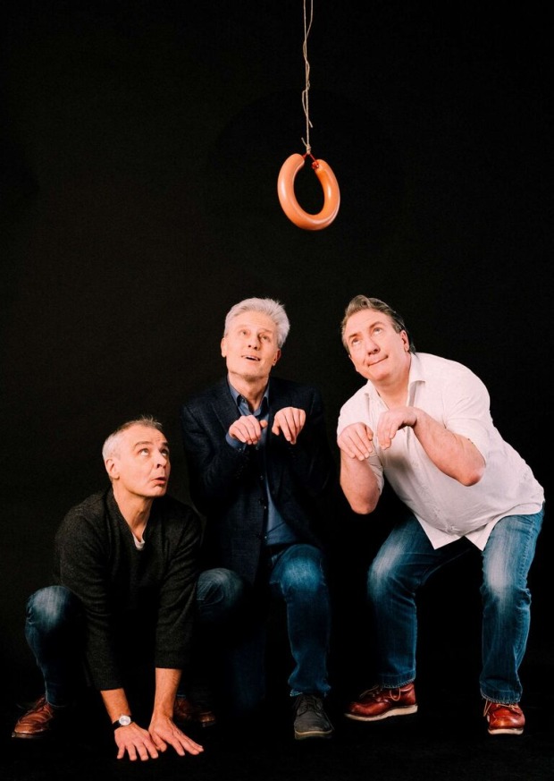 Thomas Maurer, Florian Scheuba und Robert Palfrader posieren als Staatskünstler in Hündchen-Pose vor einer, von der Decke herabhängenden Wurst.