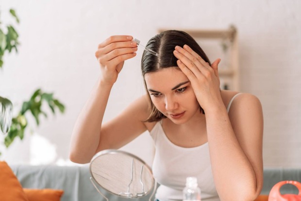 Frau träufelt sich mit einer Pipette Haaröl auf den Haaransatz
