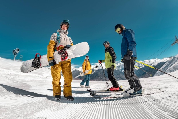 Gruppe von Snowboardern und Skifahrern stehen auf der Piste.