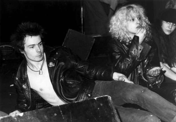 Schwarz-Weiß-Aufnahme von Sid Vicious und Nancy Spungen, die gemeinsam auf einer Konzertbühne sitzen