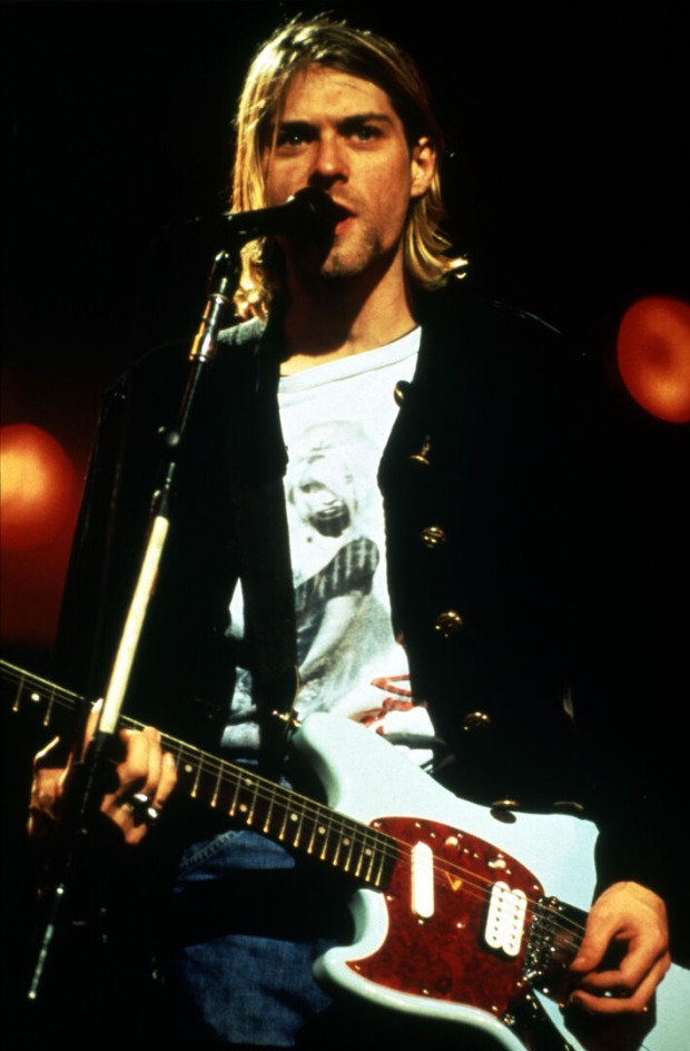 Kurt Cobain, der während eines Konzertes in ein Mikrofon singt und Gitarre spielt