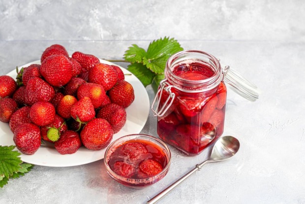 Glas mit eingelegten Erdbeeren und frischen Erdbeeren auf einem Teller