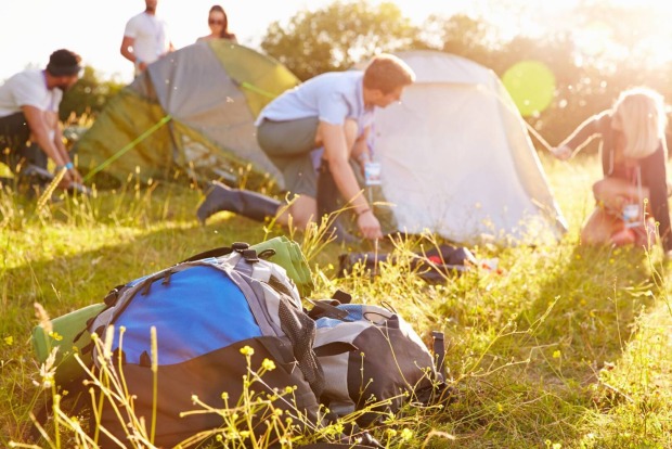 Freunde beim gemeinsamen Zeltaufbau auf einer Festivalwiese