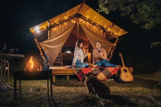 2 Frauen sitzen abends auf der Veranda eines Glamping-Zeltes und trinken gemeinsam Wein.