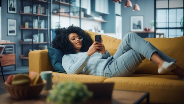 Junge Frau entspannt auf dem Sofa mit Smartphone in der Hand