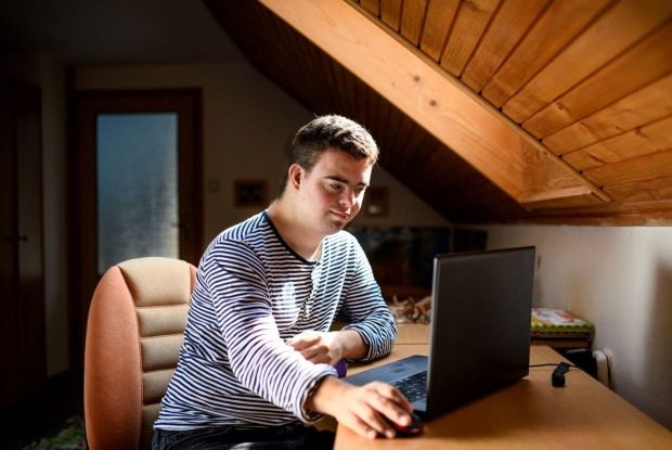 Ein junger Mann mit Down-Syndrom sitzt vor dem Laptop.